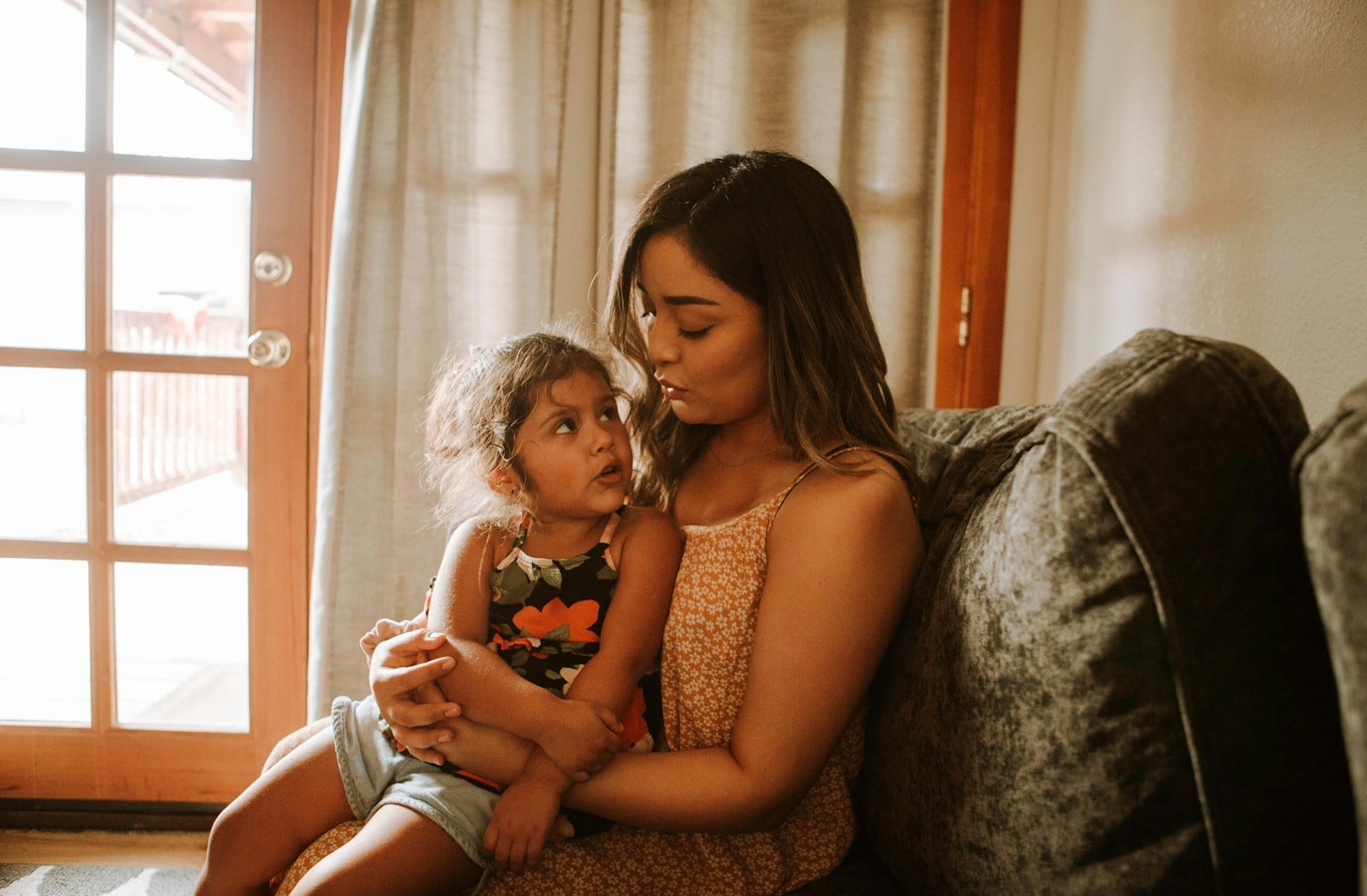 An adult and young child sitting together on a grey sofa, facing one another.