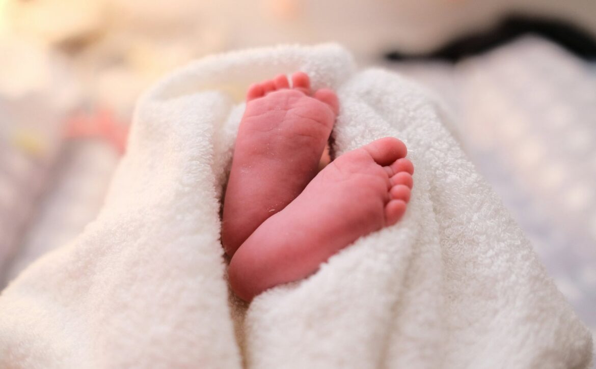 A close-up of a baby's bare feet resting against a white blanket.
