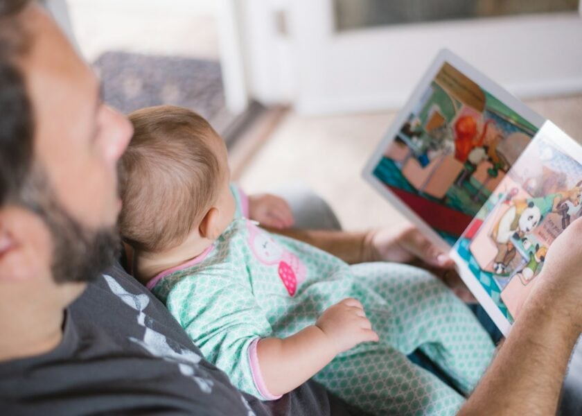 An adult holds an open picture book while a baby rests in their arms.