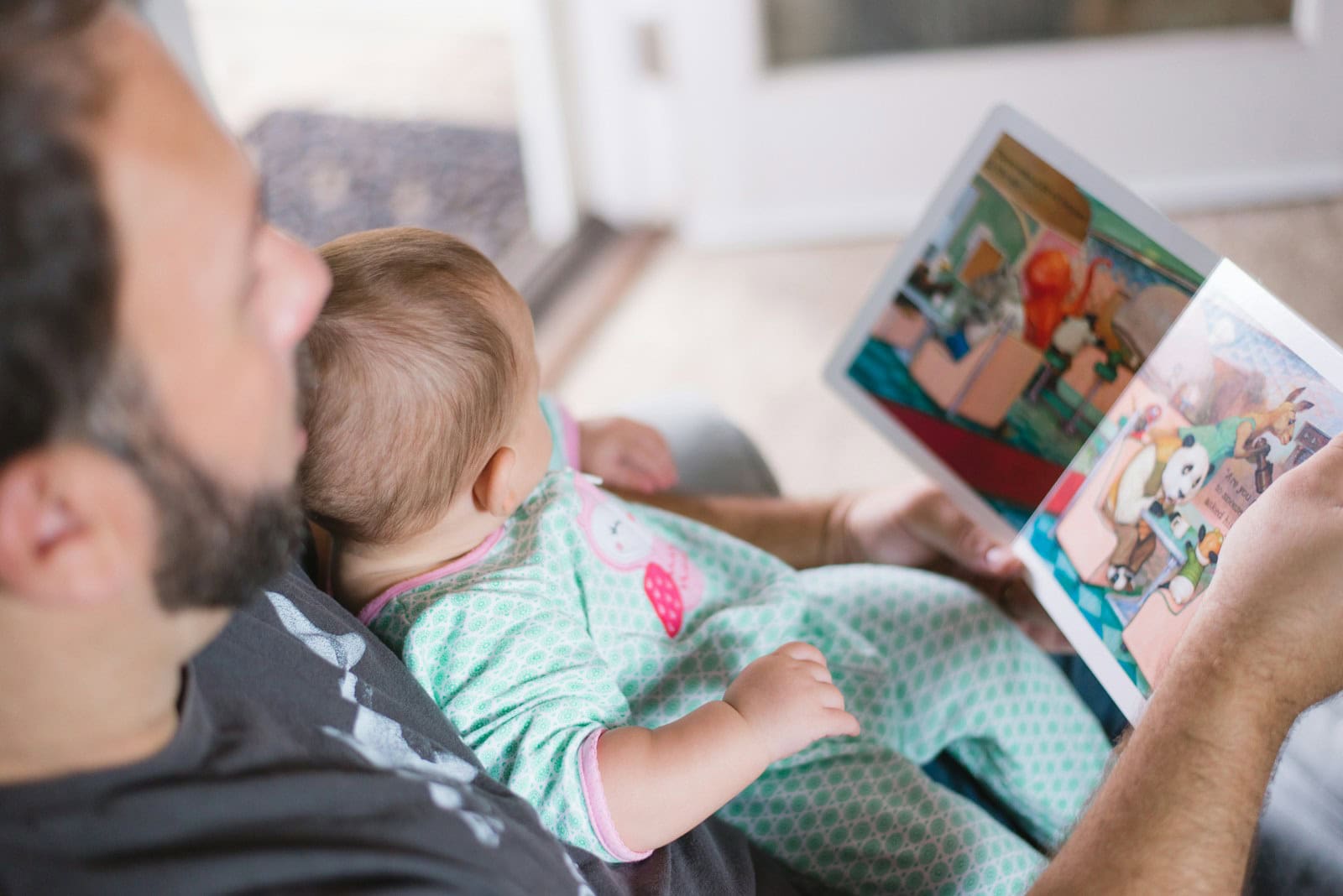 An adult holds an open picture book while a baby rests in their arms.