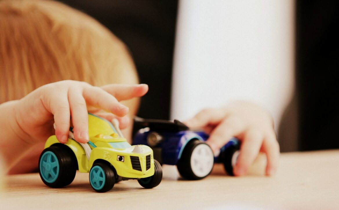 Hands moving two toy cars on a tabletop.