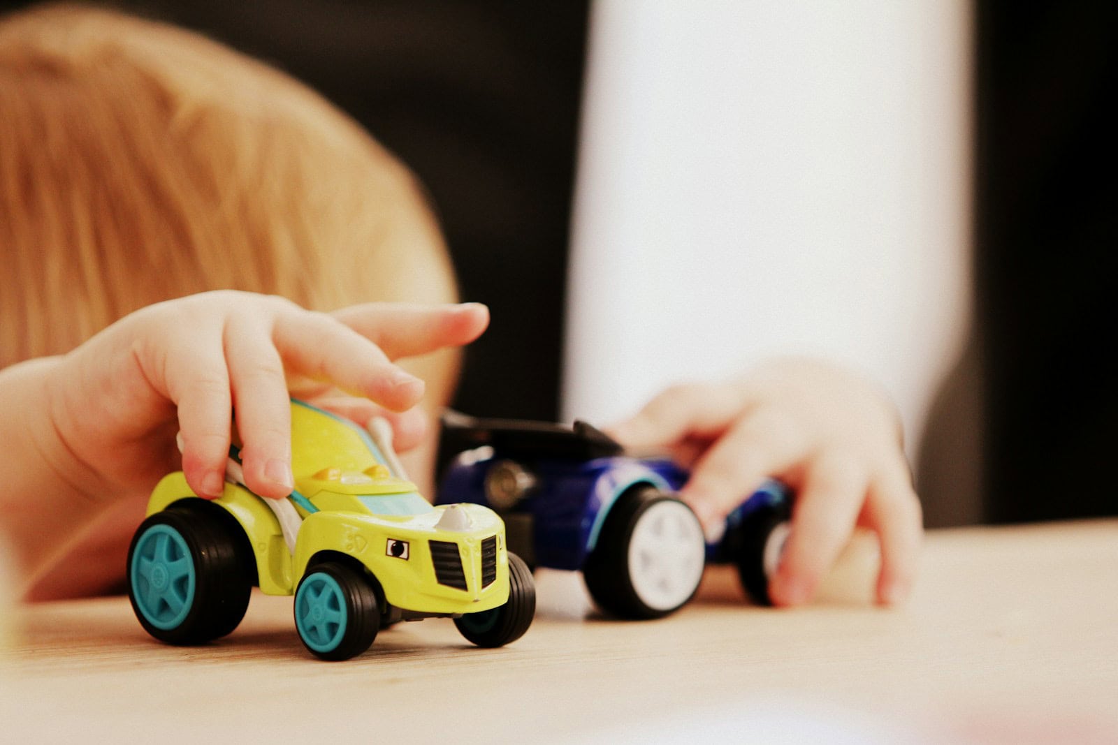 Hands moving two toy cars on a tabletop.