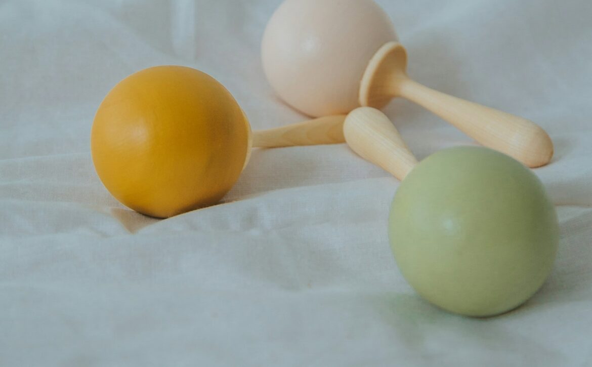 Yellow, cream and green wooden rattles resting on white fabric.