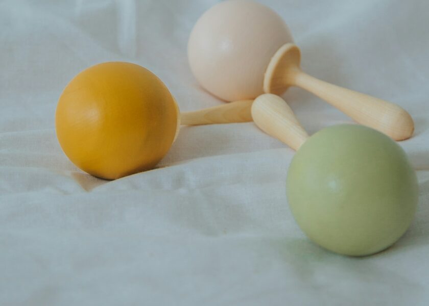 Yellow, cream and green wooden rattles resting on white fabric.