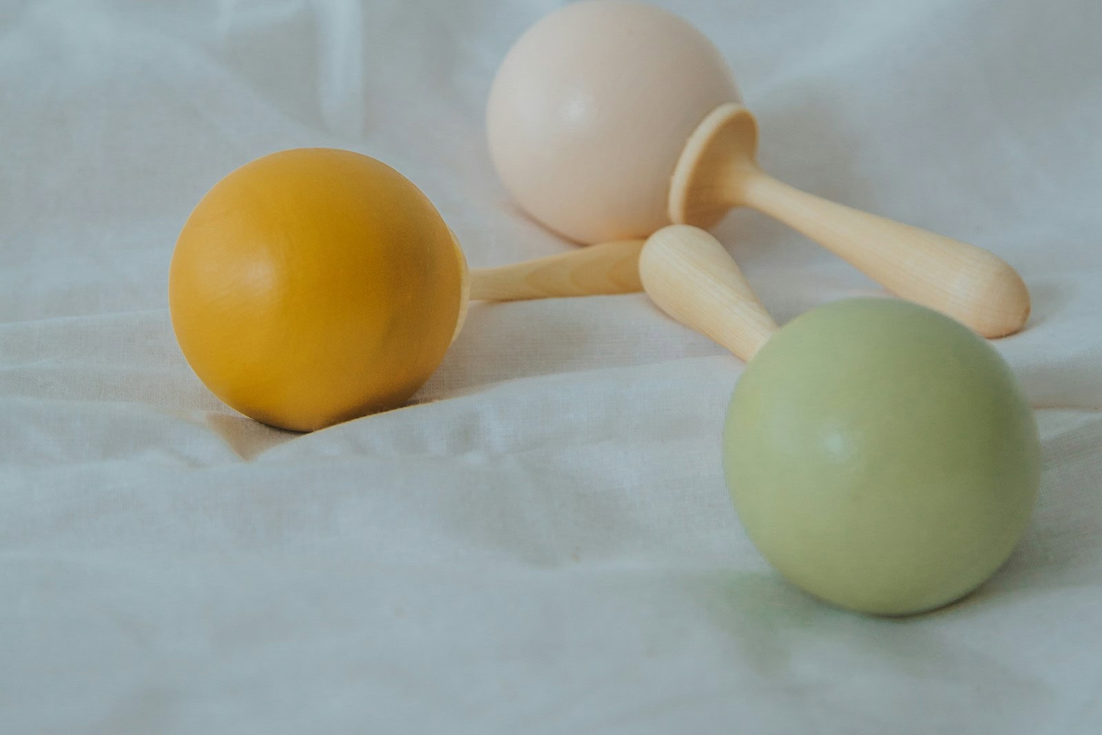 Yellow, cream and green wooden rattles resting on white fabric.