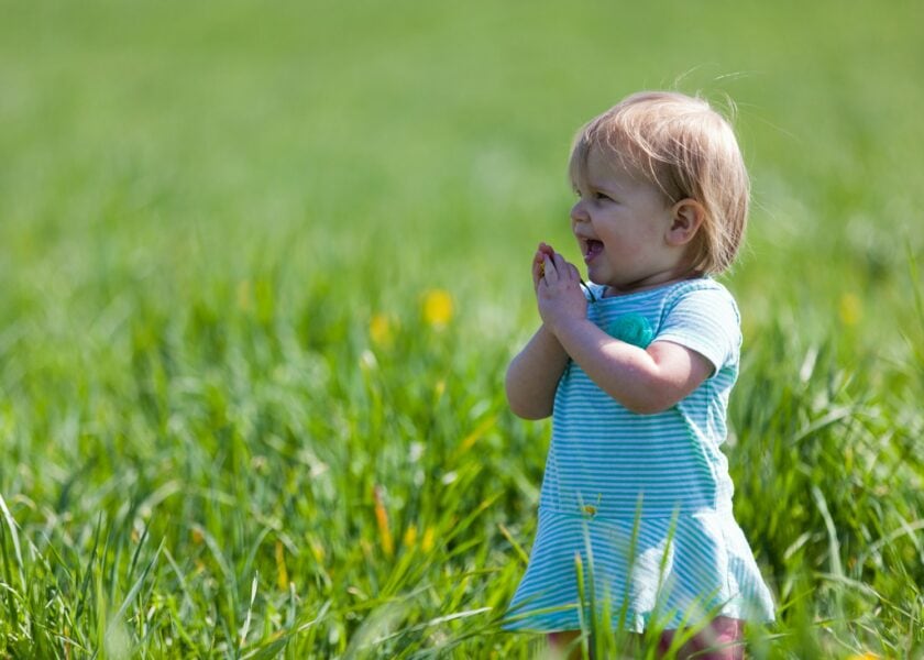 Young child in a blue striped outfit bringing their hands together in a grassy field.