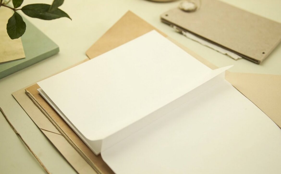 An open kraft folder holds blank cream papers on a warm tabletop, with muted green accents.
