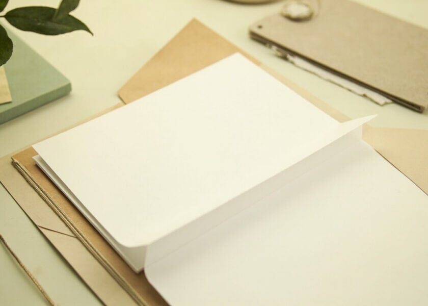 An open kraft folder holds blank cream papers on a warm tabletop, with muted green accents.