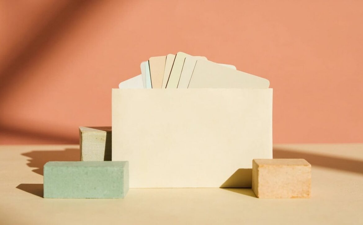 A cream envelope with blank cards emerging among muted green and natural-wood blocks on a warm tabletop.
