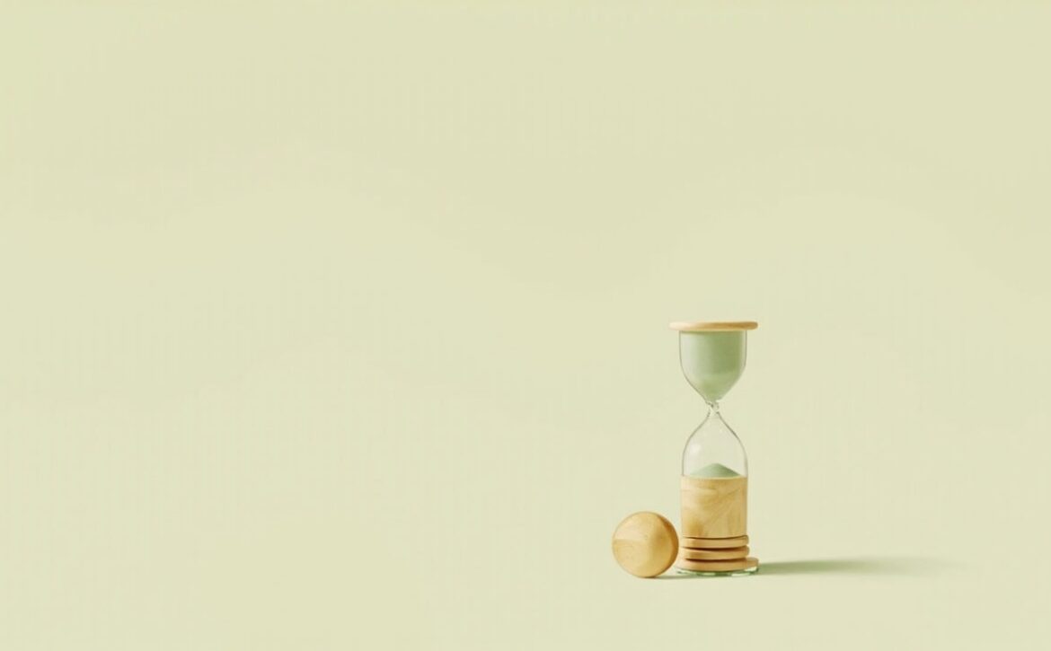 Editorial still life of a plain wooden ball beside a green-accented glass hourglass, suggesting time away from work.