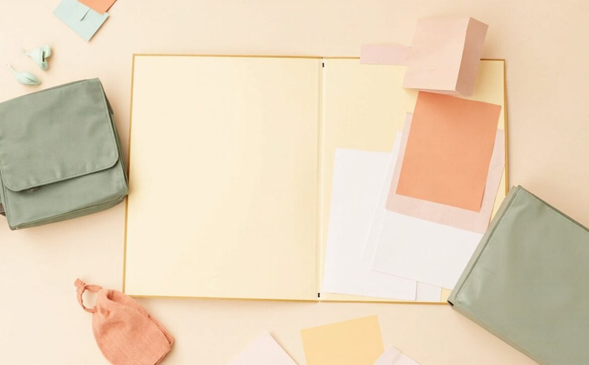 Overhead still life of an open blank cream folder, loose papers, muted sage bags and a small coral pouch.