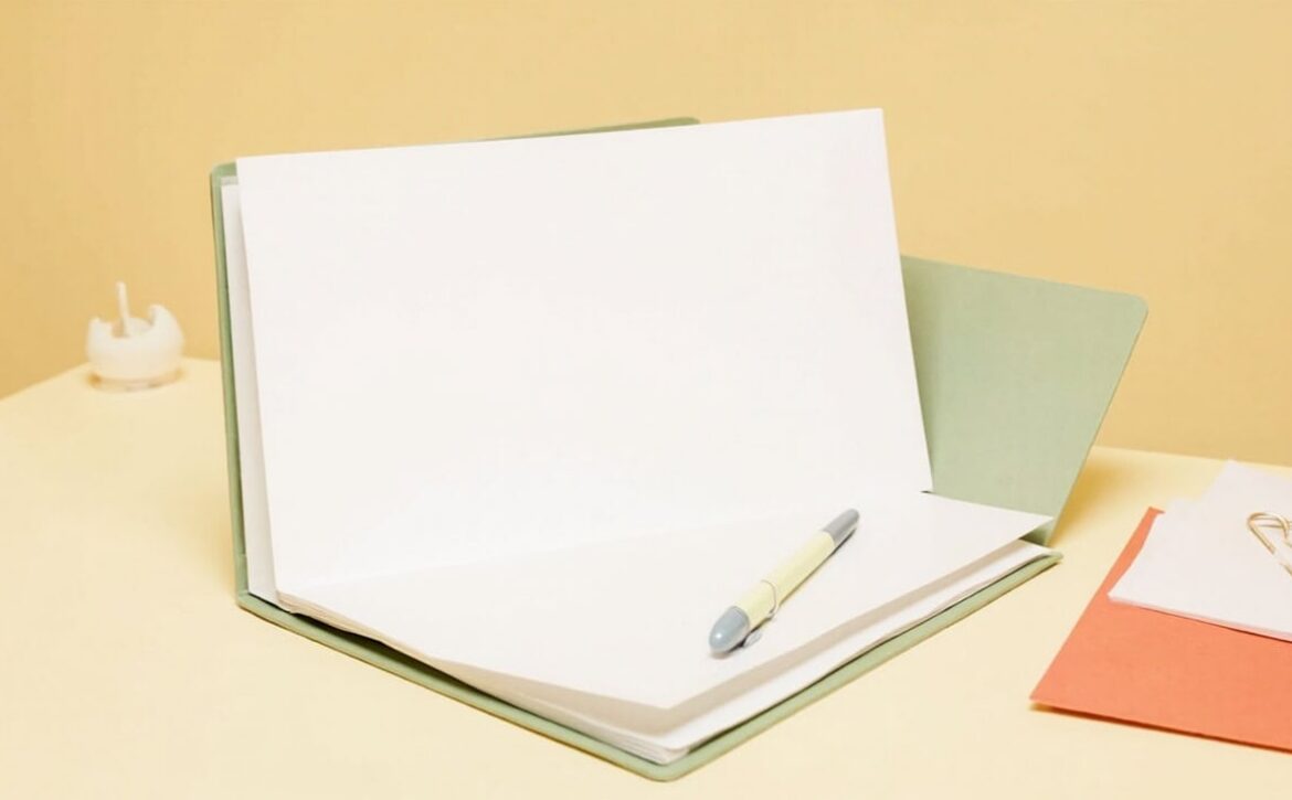 Open blank document folder with a pen, sage cover, coral papers and a gold clip on a warm cream desk.