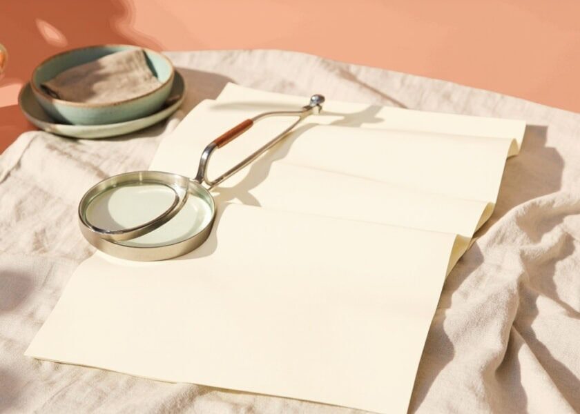 Blank papers, a stethoscope, a small bottle, eggs and ceramic dishes rest on warm linen in soft sunlight.