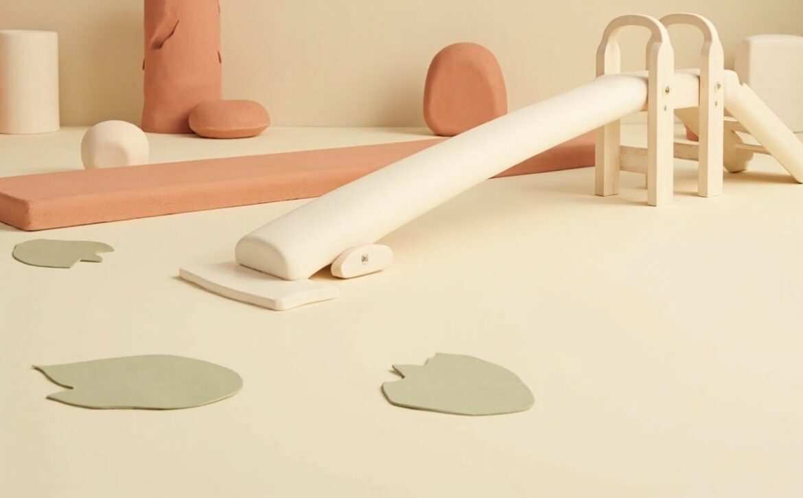 A cream-and-coral still life of an unmarked low balance beam, small climbing frame and slide, with leaf-shaped stepping pads.