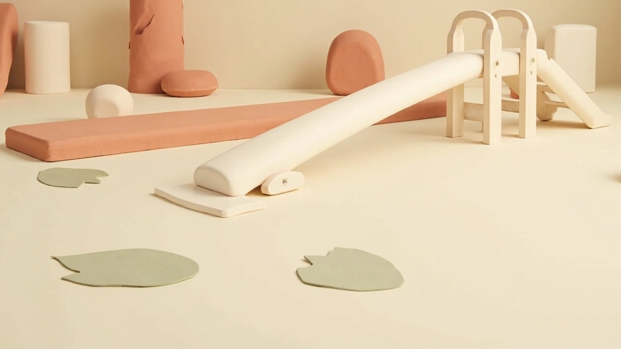 A cream-and-coral still life of an unmarked low balance beam, small climbing frame and slide, with leaf-shaped stepping pads.