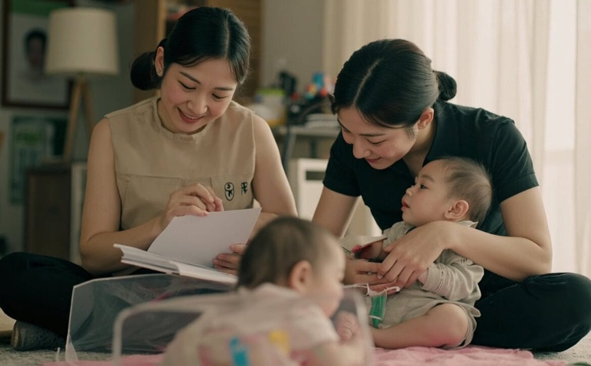 Disclosed AI illustration of a parent and childminder reviewing a plain note while an awake infant plays safely in a Singapore living room