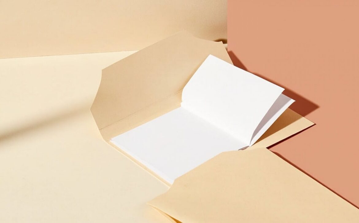 Open plain folder with blank white sheets and neutral envelopes on a warm cream and coral tabletop.