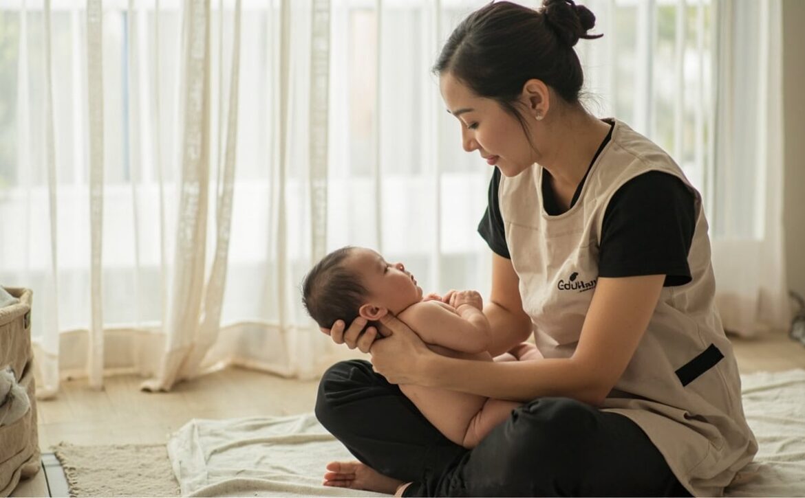 A childminder supports an awake newborn against her chest while watching the baby's face