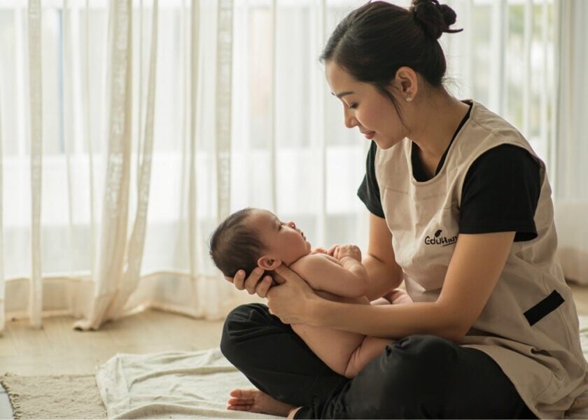 A childminder supports an awake newborn against her chest while watching the baby's face