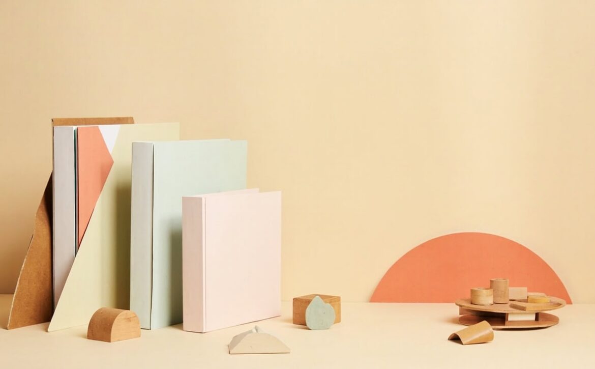 Pastel folders, wooden geometric pieces and a coral arch decorate a cream table in a warm, minimal still life.
