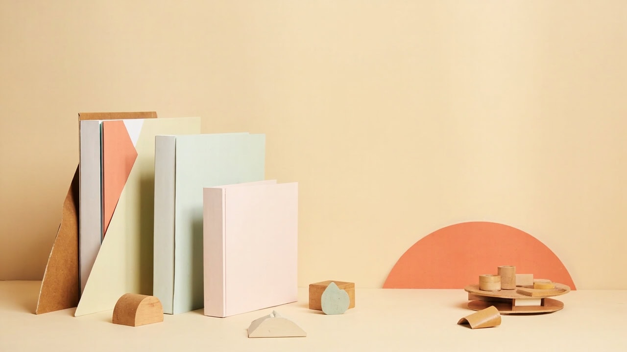 Pastel folders, wooden geometric pieces and a coral arch decorate a cream table in a warm, minimal still life.