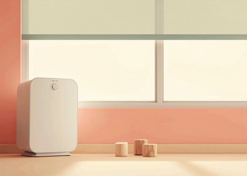 A generic white portable air purifier stands beside a closed window, with plain wooden blocks on a warm cream floor.