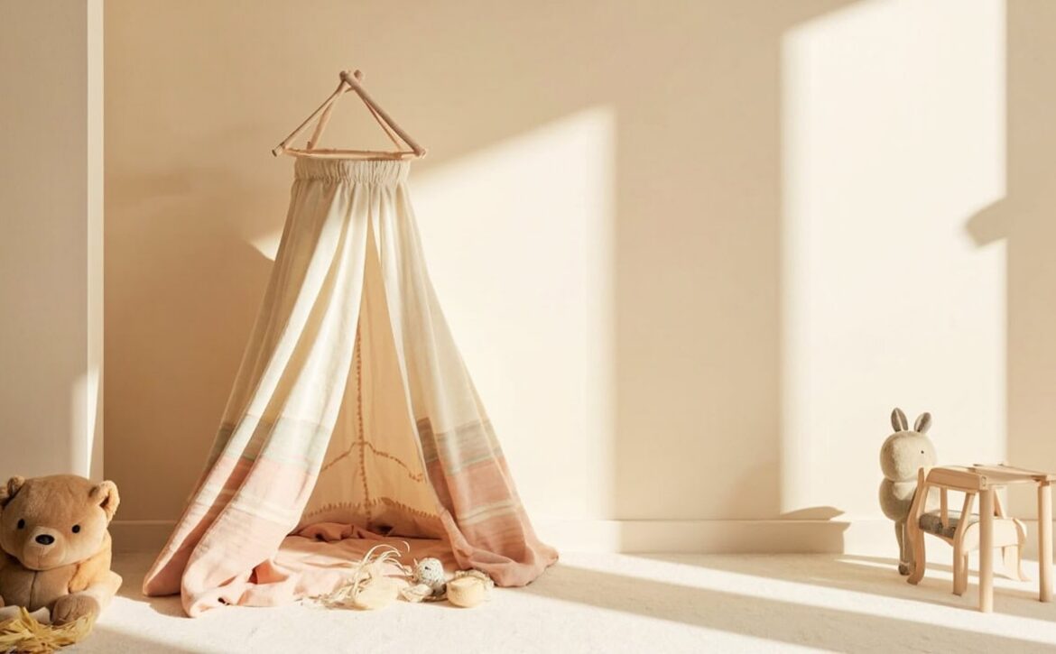 A cream fabric play canopy in a sunlit neutral room, beside a teddy, scattered toys, a plush rabbit and miniature wooden furniture.