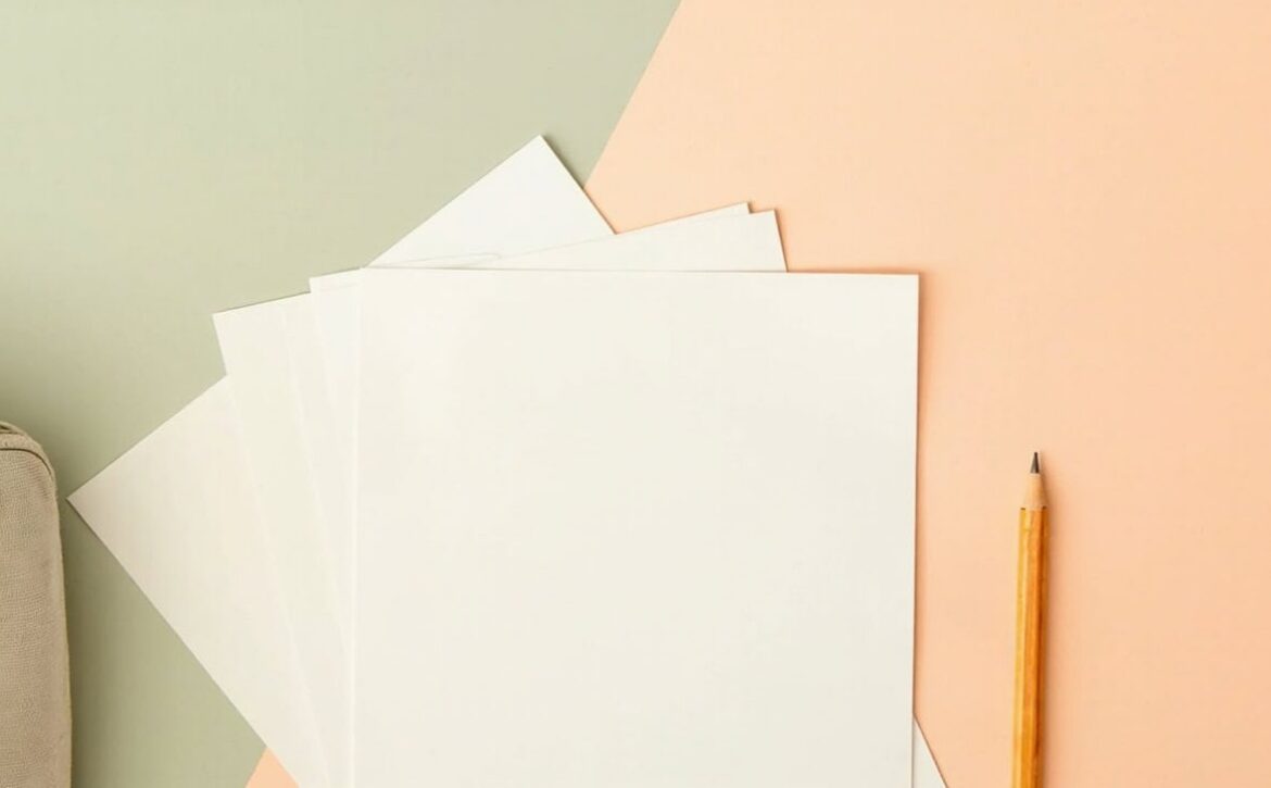 Blank sheets fanned beside a yellow pencil and a cropped, unbranded beige satchel on a sage-and-coral background.