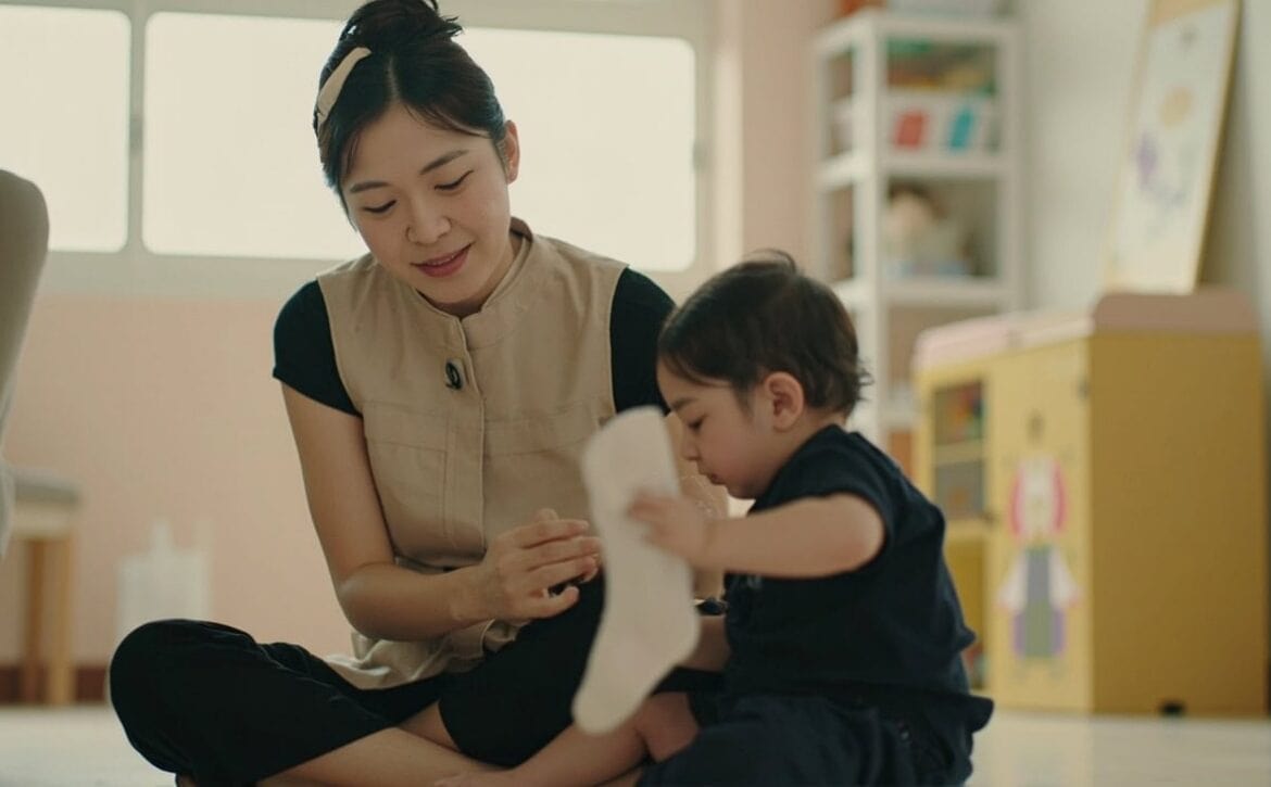 Childminder watches as an infant reaches for a sock