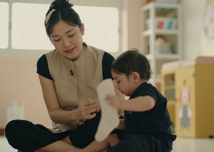 Childminder watches as an infant reaches for a sock