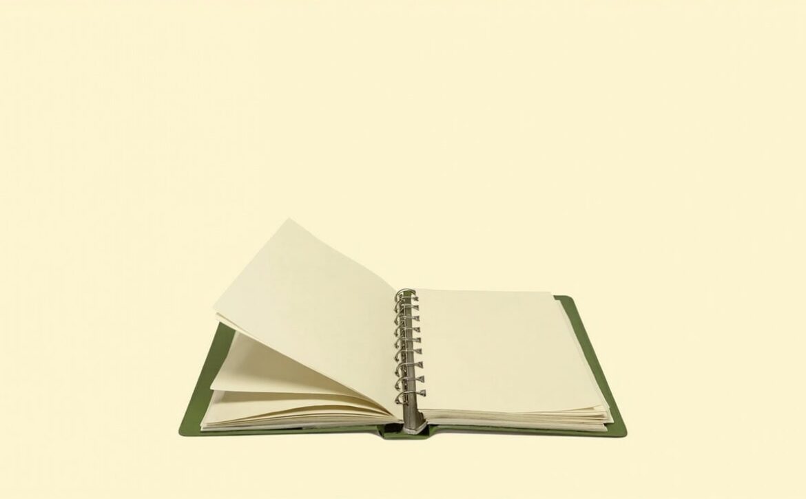 An open muted-green ring binder with blank cream pages sits alone on a warm ivory background.