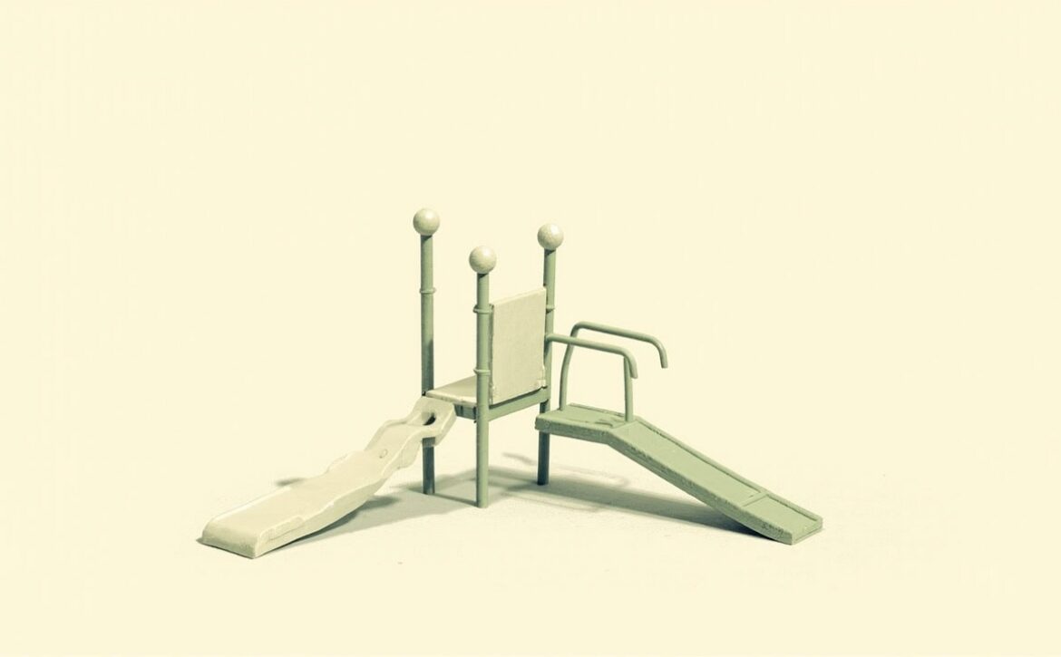 Stylised empty modular playground with a small slide, raised platform, rails and sloping ramp on a plain ivory background.