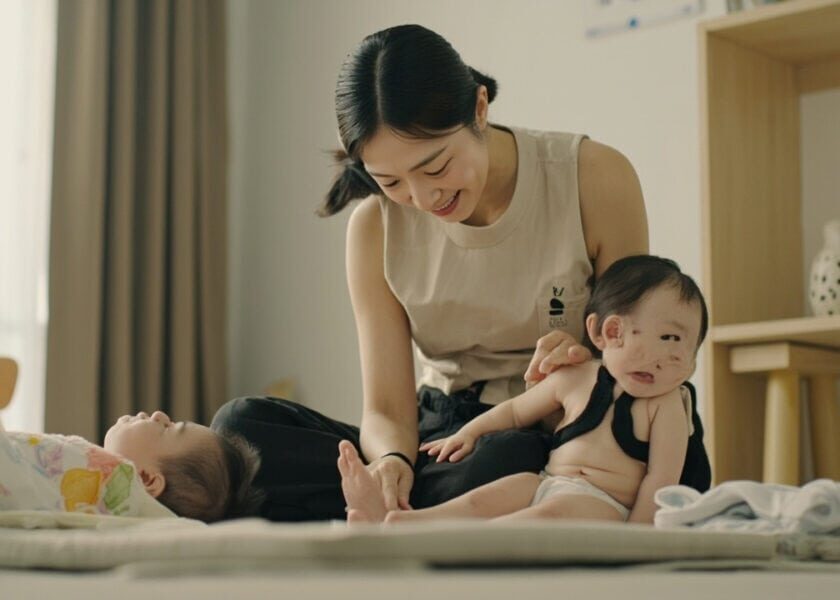 Childminder acknowledges two infants during shared floor play